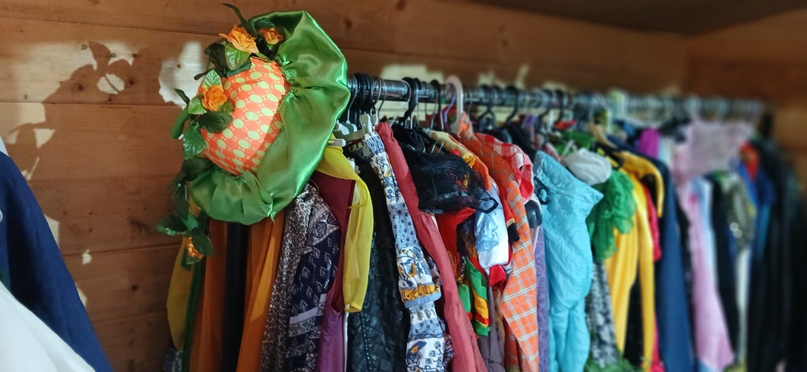 Portant de costumes de théâtre serrés sur leurs cintres dans la cabane, avec un chapeau vert et orange fleuri au premier plan