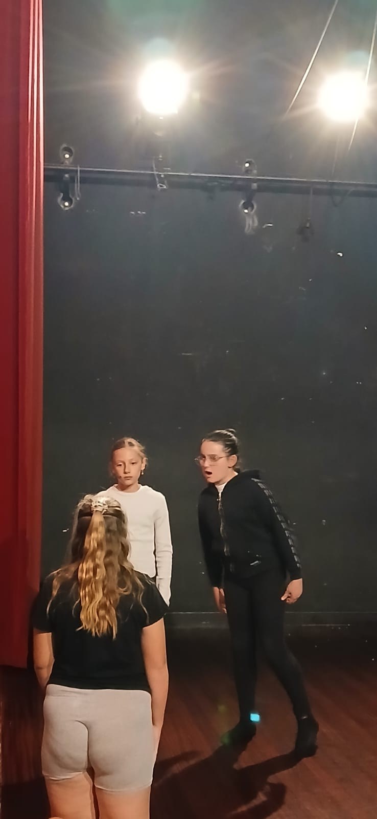 Trois jeunes comédiennes en scène sous un projecteur, devant un rideau rouge