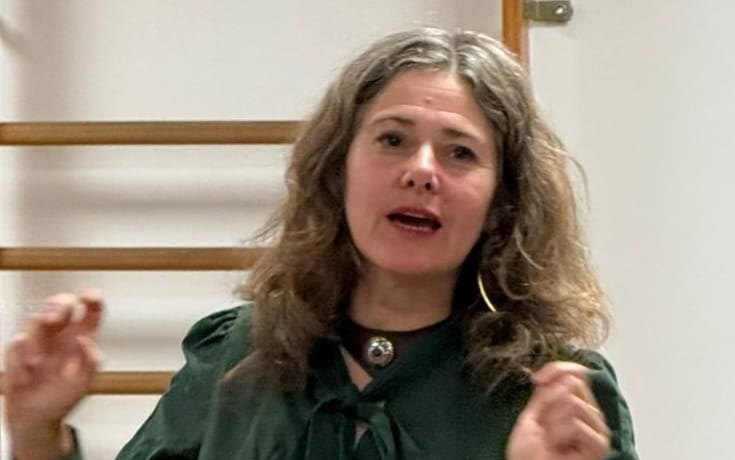 Une comédienne parle, les mains levées, devant un mur d'espaliers