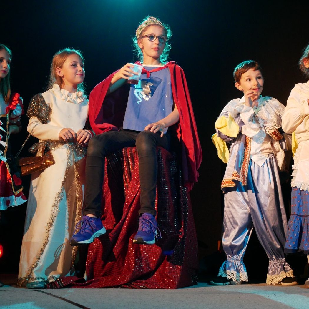 Jeunes comédiens costumés sur scène, l'un porte une couronne et une cape rouge