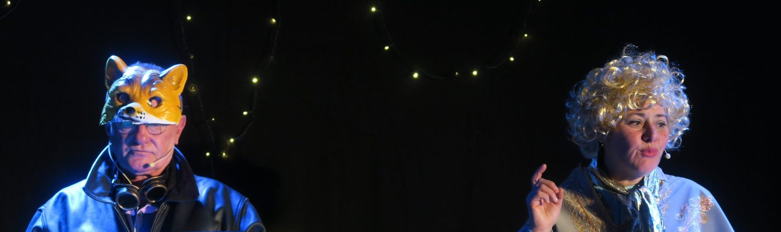 Deux comédiens en scène, l'un masqué en renard, sous une guirlande lumineuse