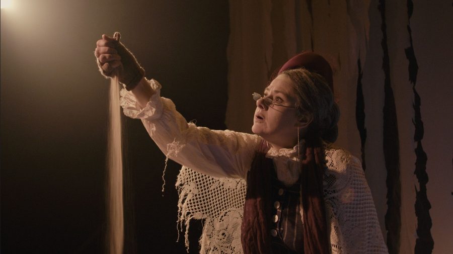 La comédienne de La Pluie seule en scène, en costume, devant des rideaux de toile déchirée