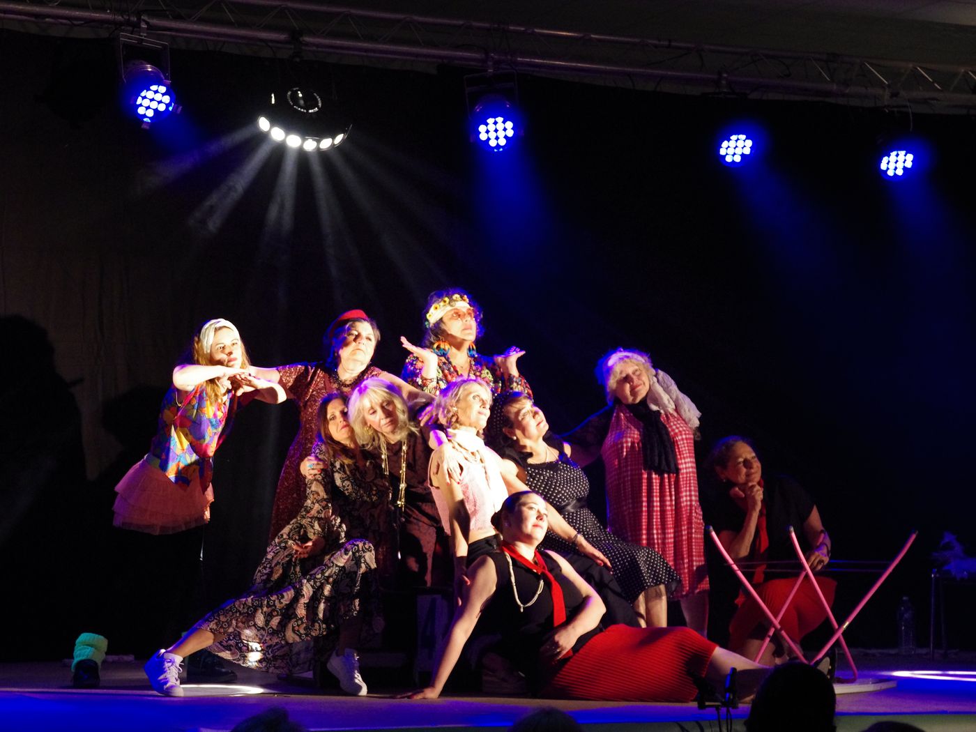 Un groupe d'élèves adultes en costumes, groupés sur le plateau sous des projecteurs bleus